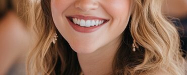 A bride-to-be with glowing skin, soft pink lips, and delicate eye makeup smiling at her bridal shower, surrounded by flowers and friends.