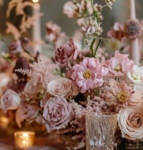 A beautifully decorated wedding table featuring dusty pink flowers, candles, and elegant dinnerware, creating a romantic ambiance.
