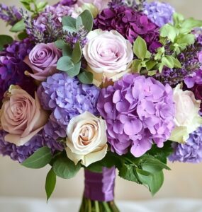 A beautifully arranged wedding bouquet featuring various purple flowers, including roses, lavender, and hydrangeas, set against a soft, romantic background.