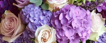 A beautifully arranged wedding bouquet featuring various purple flowers, including roses, lavender, and hydrangeas, set against a soft, romantic background.