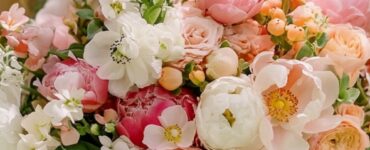 A bride holding a fresh spring wedding bouquet filled with seasonal flowers in shades of pink, white, and peach, with lush greenery.