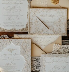 A collection of vintage wedding invitations featuring elegant lace, gold foiling, and antique-style calligraphy, set on a rustic wooden background.