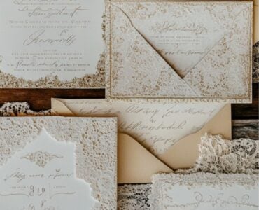 A collection of vintage wedding invitations featuring elegant lace, gold foiling, and antique-style calligraphy, set on a rustic wooden background.